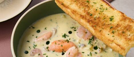 A bowl of creamy seafood soup garnished with herbs, accompanied by a toasted bread slice.