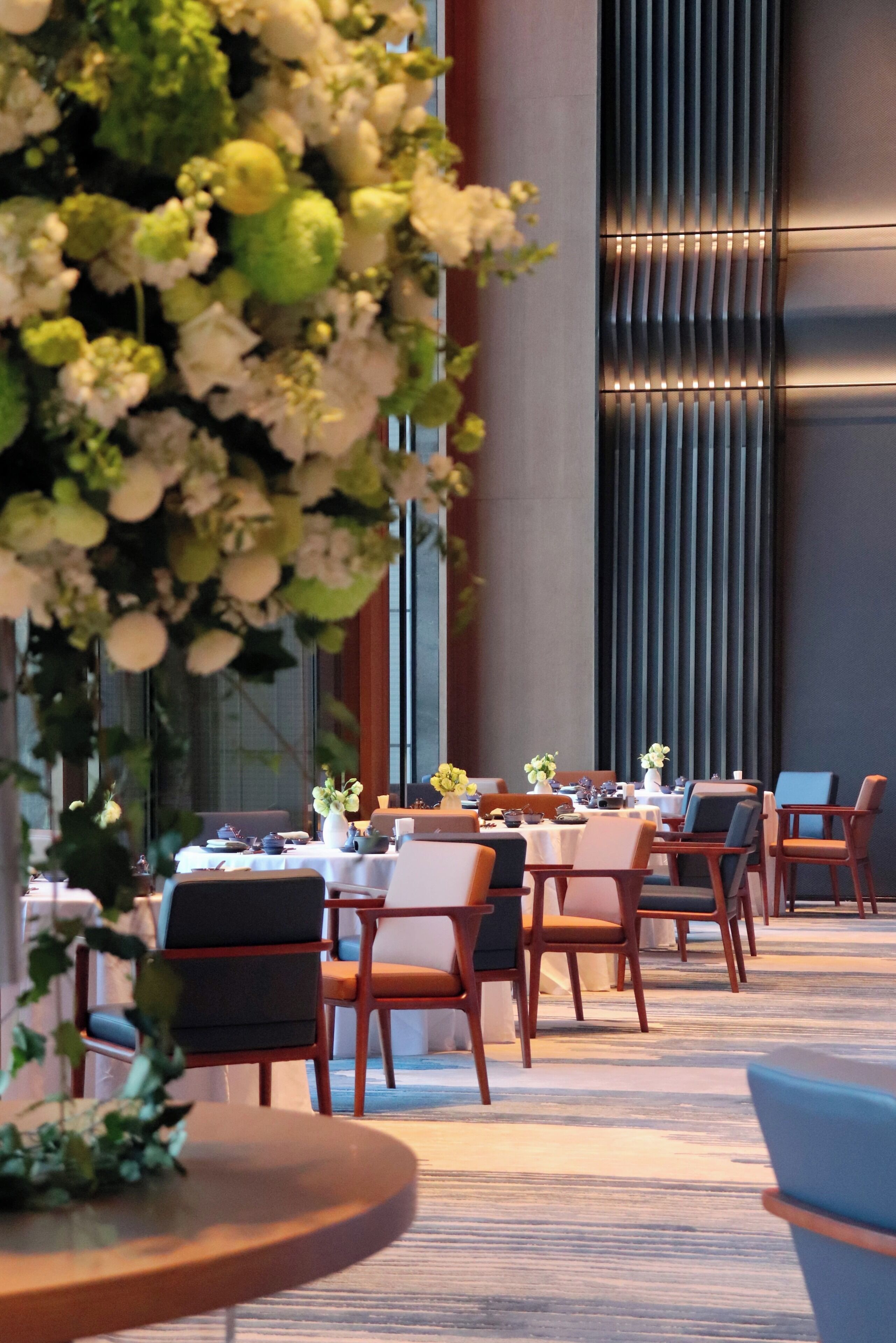A dining area with tables and chairs, a large decorative plant, and a modern wall with vertical lines.