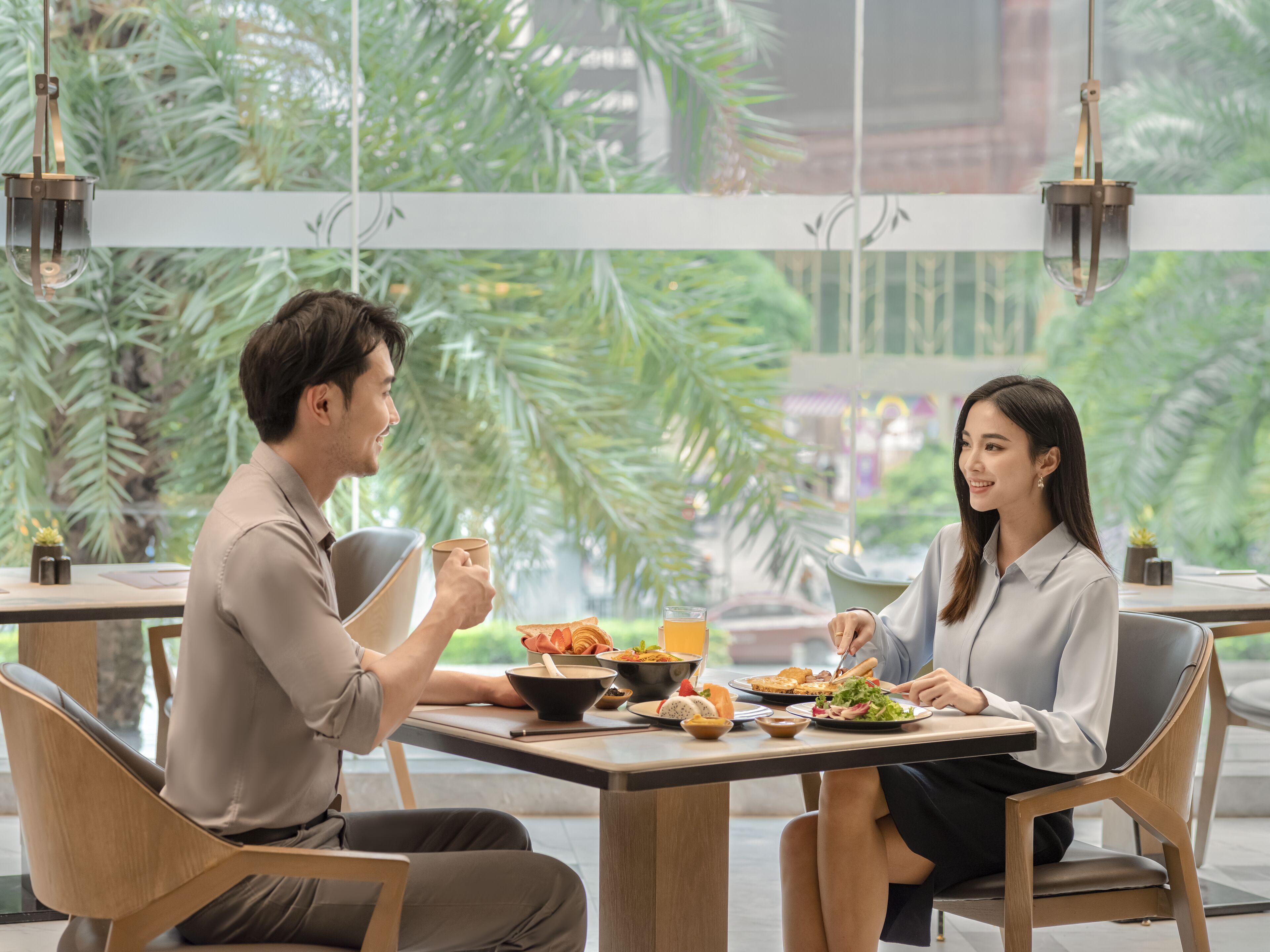 A dining area with tables and chairs, a window with a view of greenery, and hanging lights.