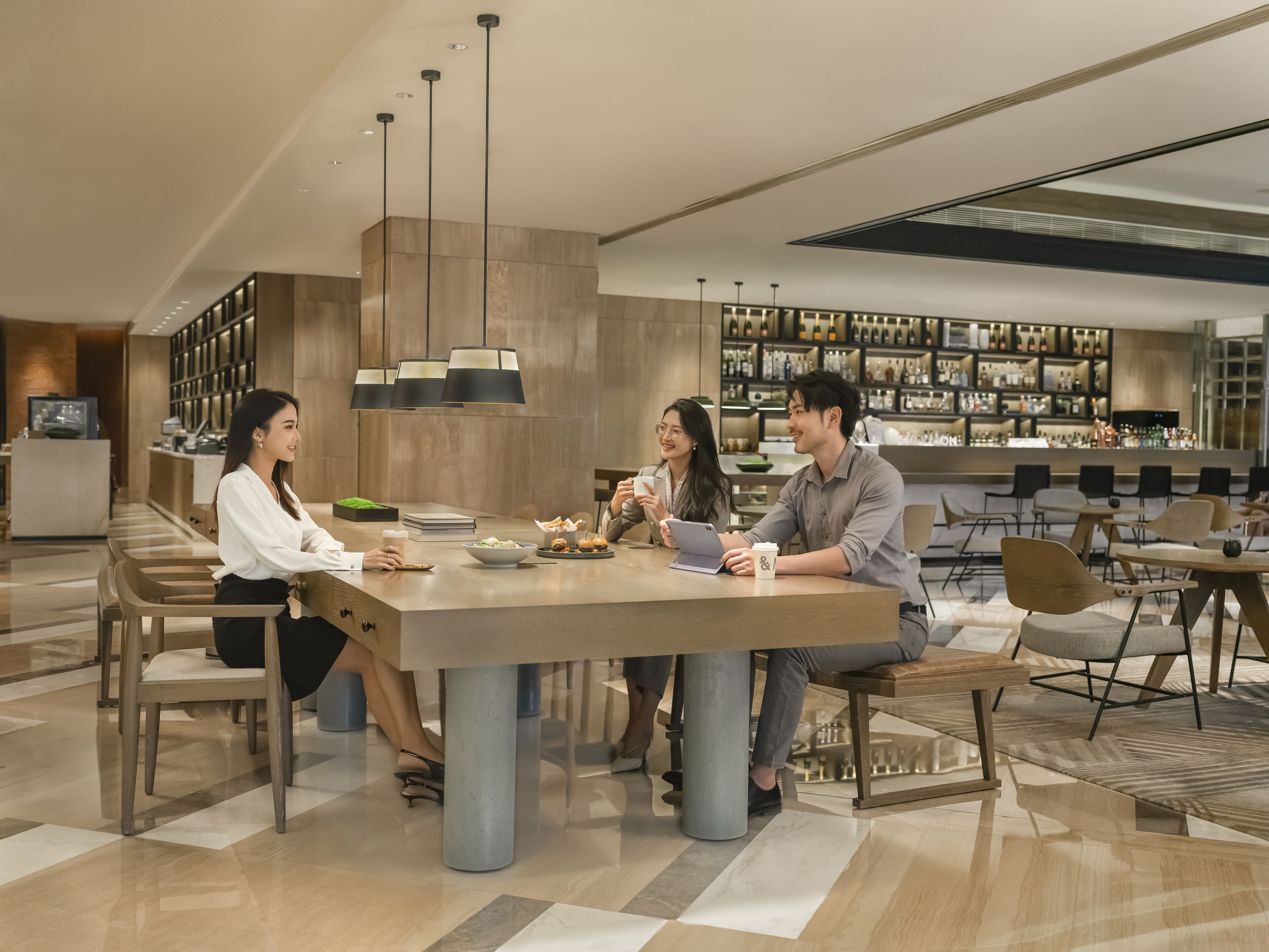 A modern dining area with a long table, multiple chairs, and a bar in the background.