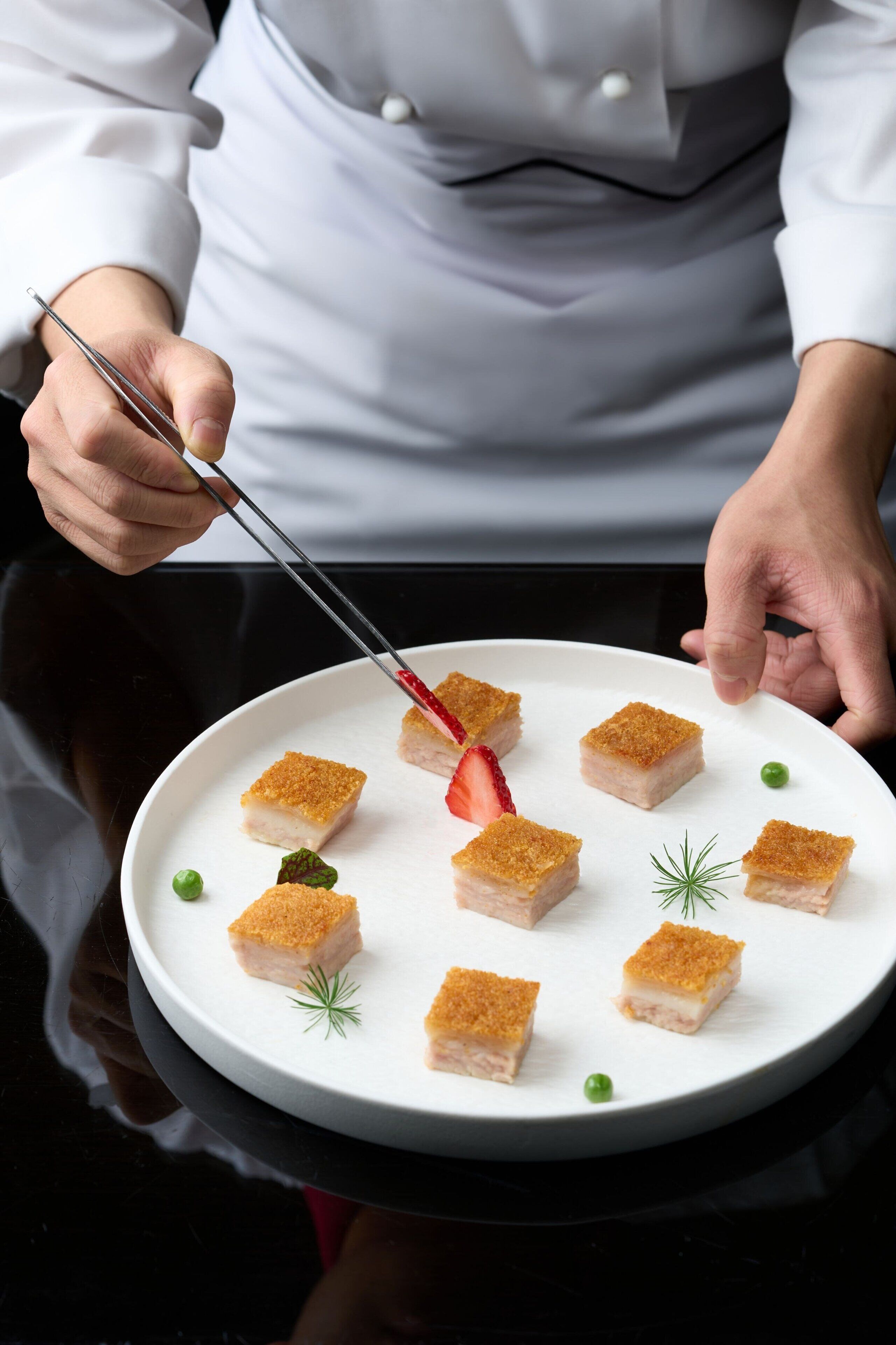 A chef holding tongs over a plate of food.