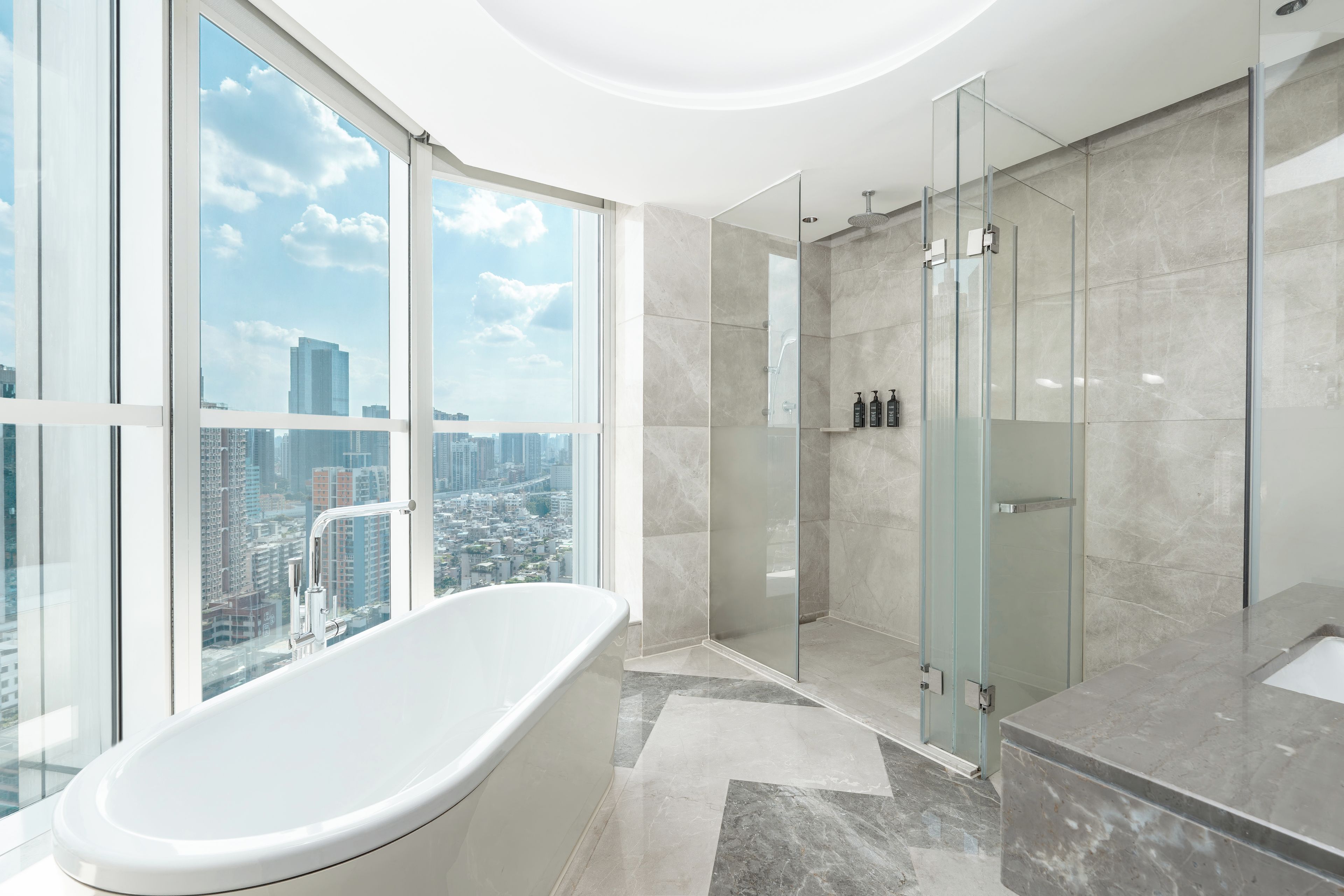 A modern bathroom with a bathtub, glass shower enclosure, and a city view.