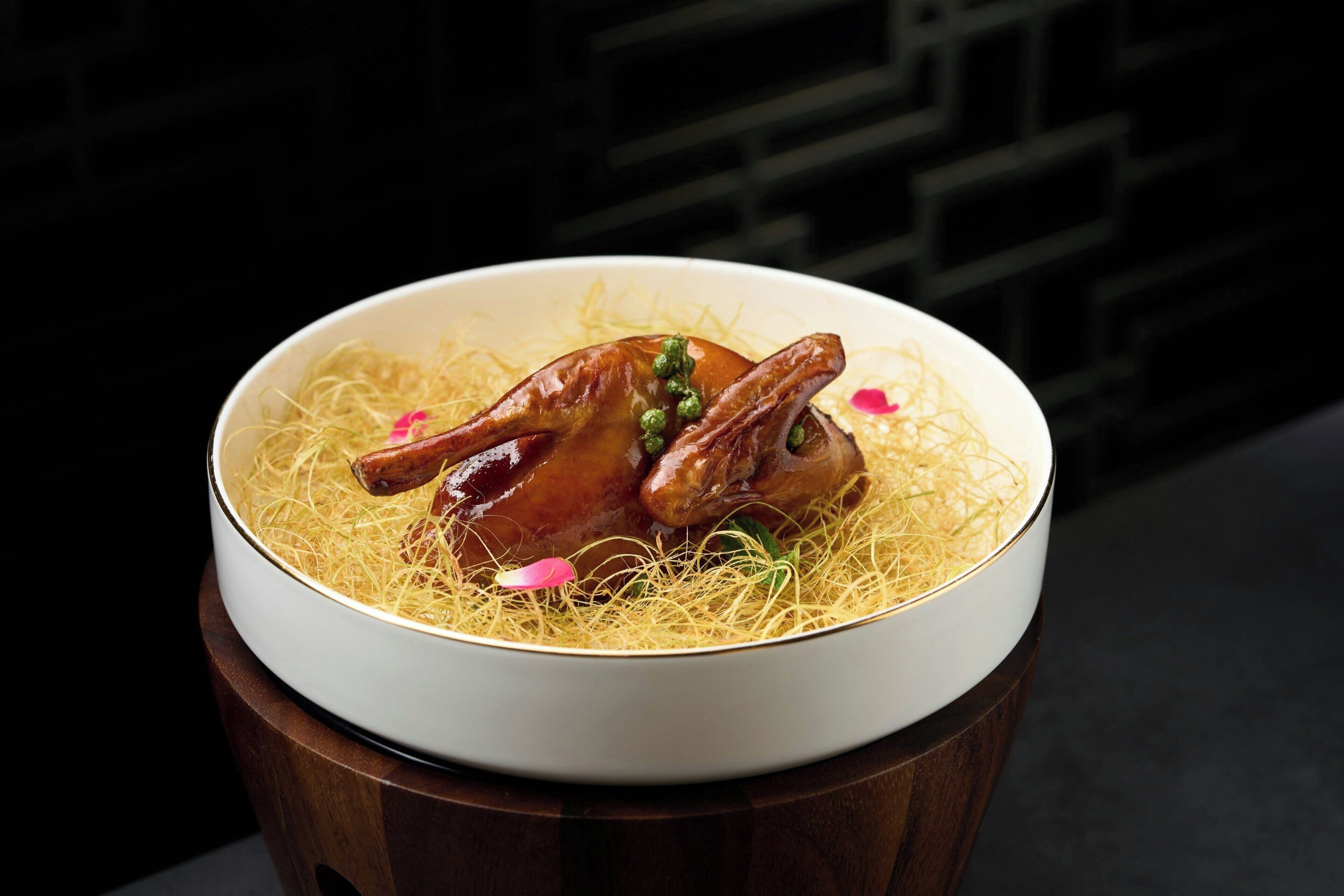 A bowl of food with noodles and two pieces of meat, possibly chicken, on a wooden table.