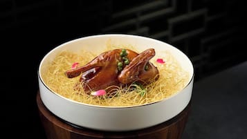 A bowl of food with noodles and two pieces of meat, possibly chicken, on a wooden table.