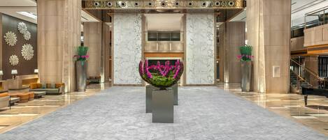 Eine geräumige Lobby mit einer zentralen Blumenkomposition, Marmorböden und einer hohen Decke mit Kronleuchtern.