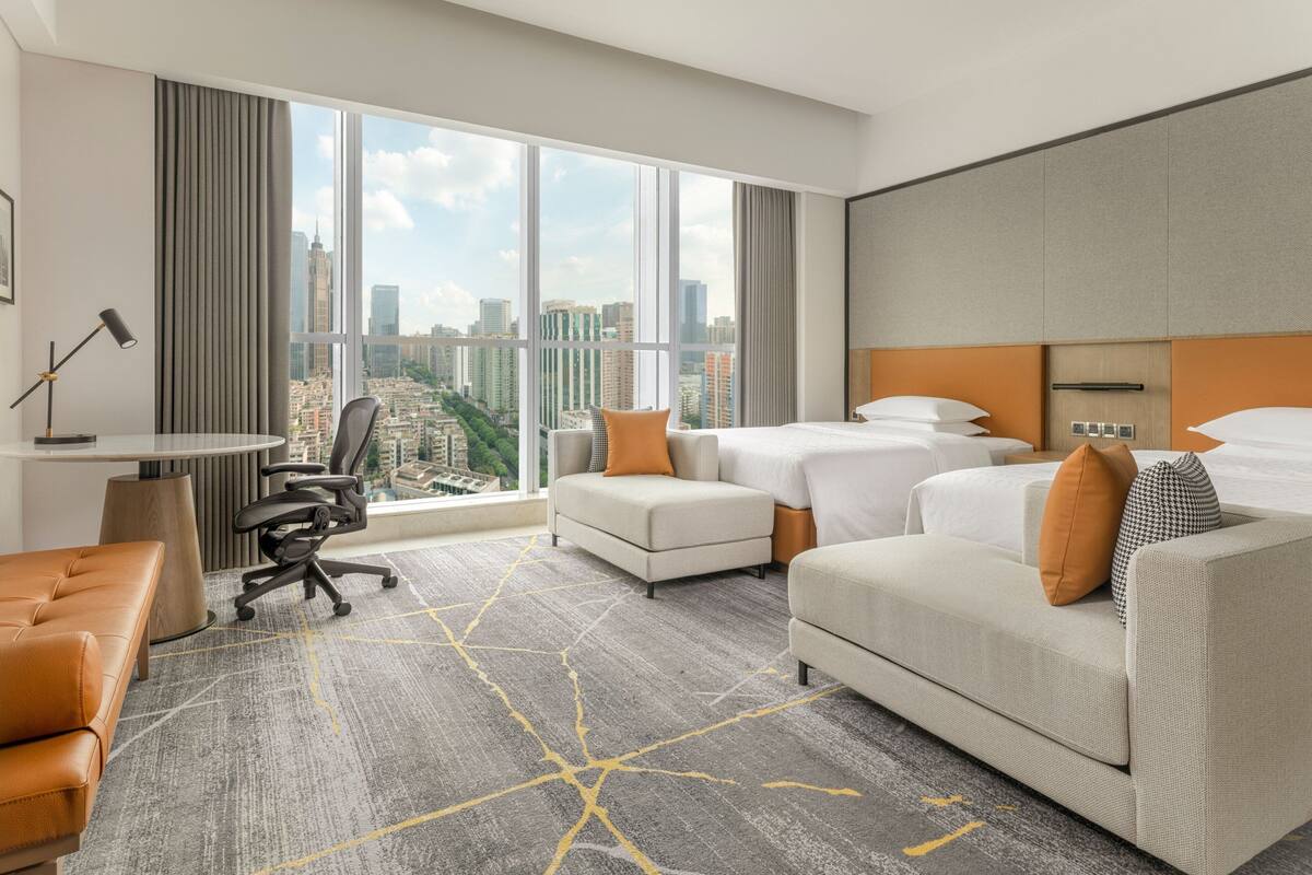 A hotel room with a large window, a sofa, a bed, and a desk.