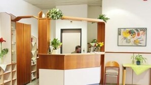 A reception area with a wooden reception desk, a chair, a small table with a plant, and a painting on the wall. - Hotel Karwendel (Innsbruck)