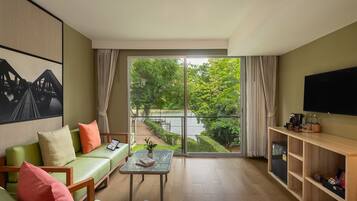 A living room with a sofa, a coffee table, a TV, and a view of a bridge and greenery.
