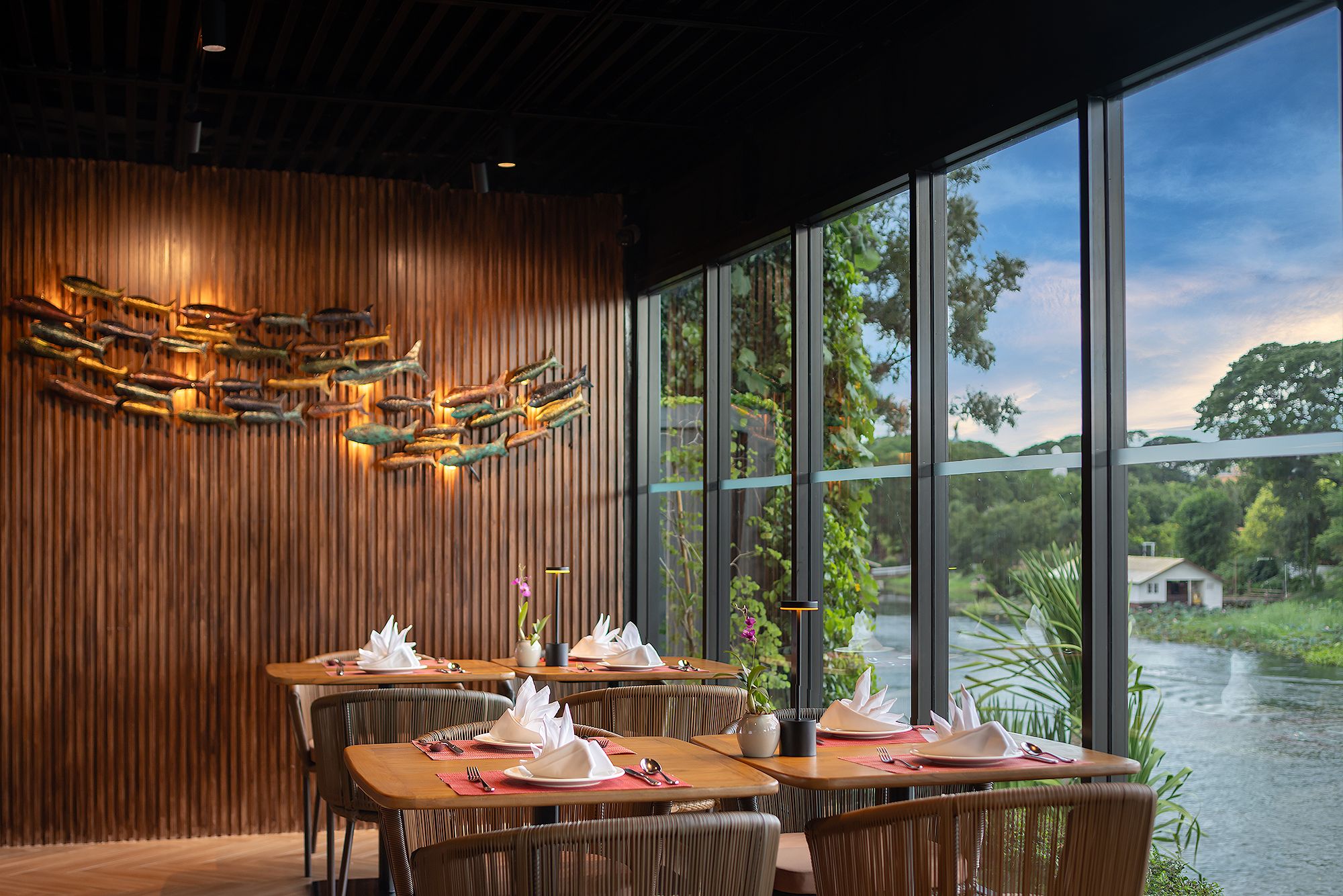 Un restaurante con paredes de madera, un ventanal grande con vista al río y un comedor con mesas preparadas para dos.