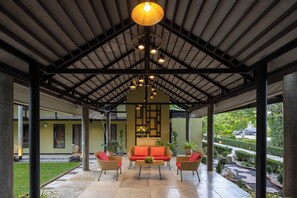A covered outdoor seating area with a sofa, chairs, and a table, under a high ceiling with exposed beams and hanging lights. - U Inchantree Kanchanaburi (Kanchanaburi)