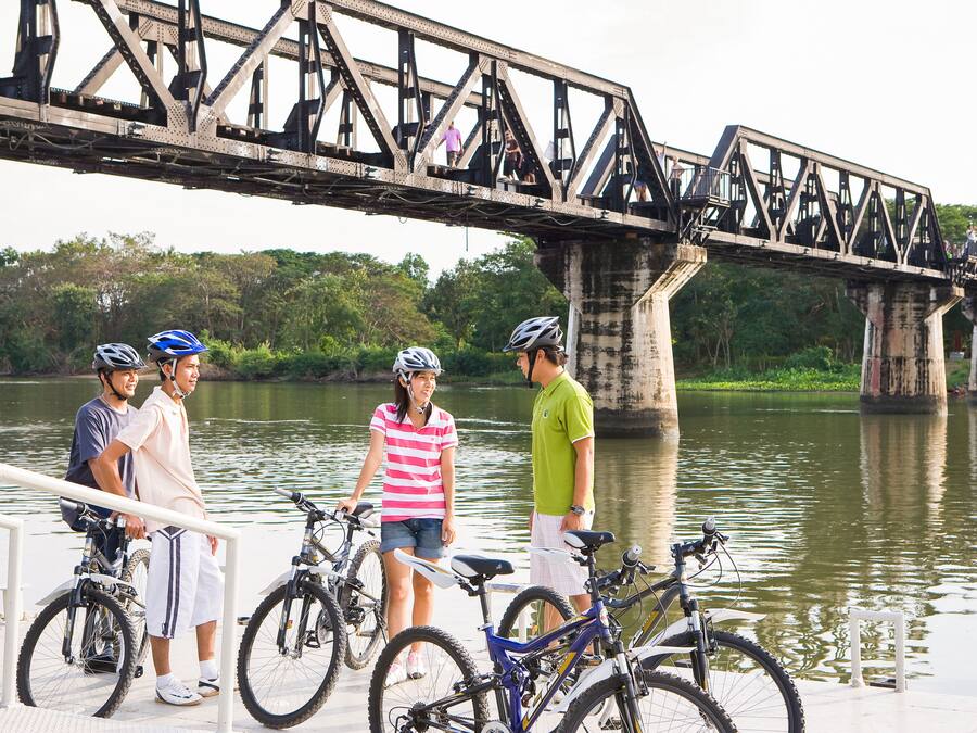 A group of people standing by bicycles near a bridge over water.