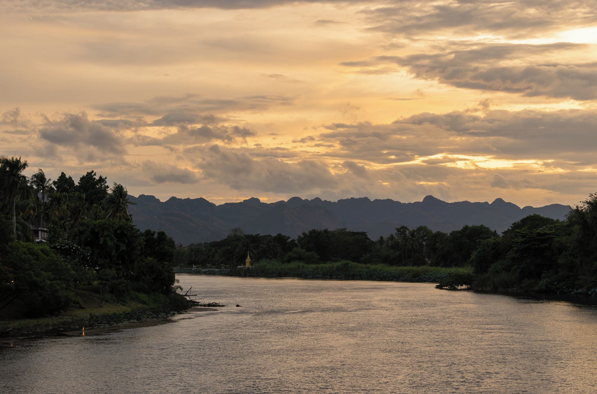 A river with mountains in the background and a structure on the left bank.