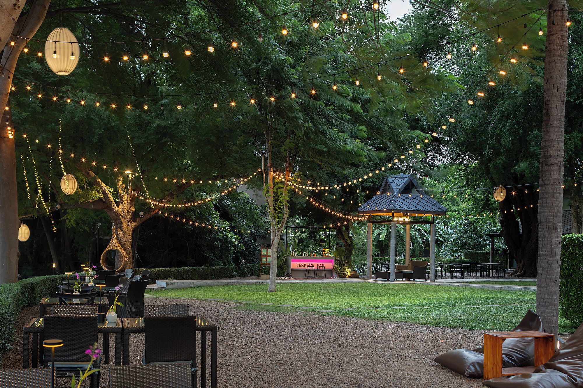 Un'area salotto all'aperto con tavoli, sedie, un gazebo e luci decorative.
