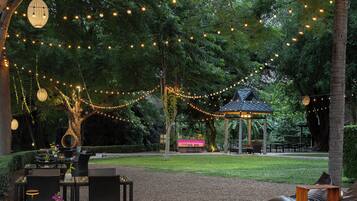 Un'area salotto all'aperto con tavoli, sedie, un gazebo e luci decorative.