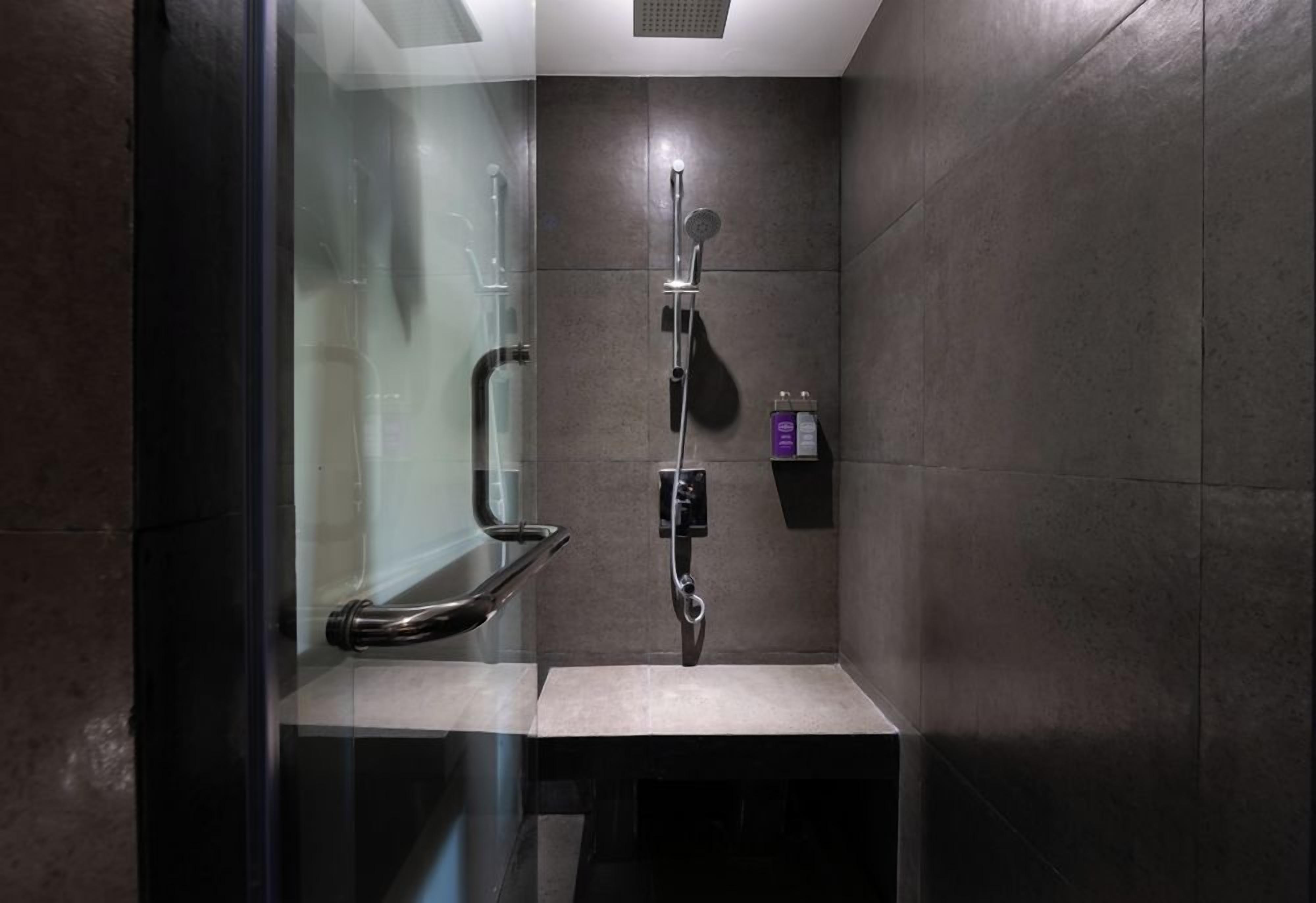 Ein modernes Duschbad mit Glastrennwand, Handbrause, Armatur an der Wand und Seifenspender.