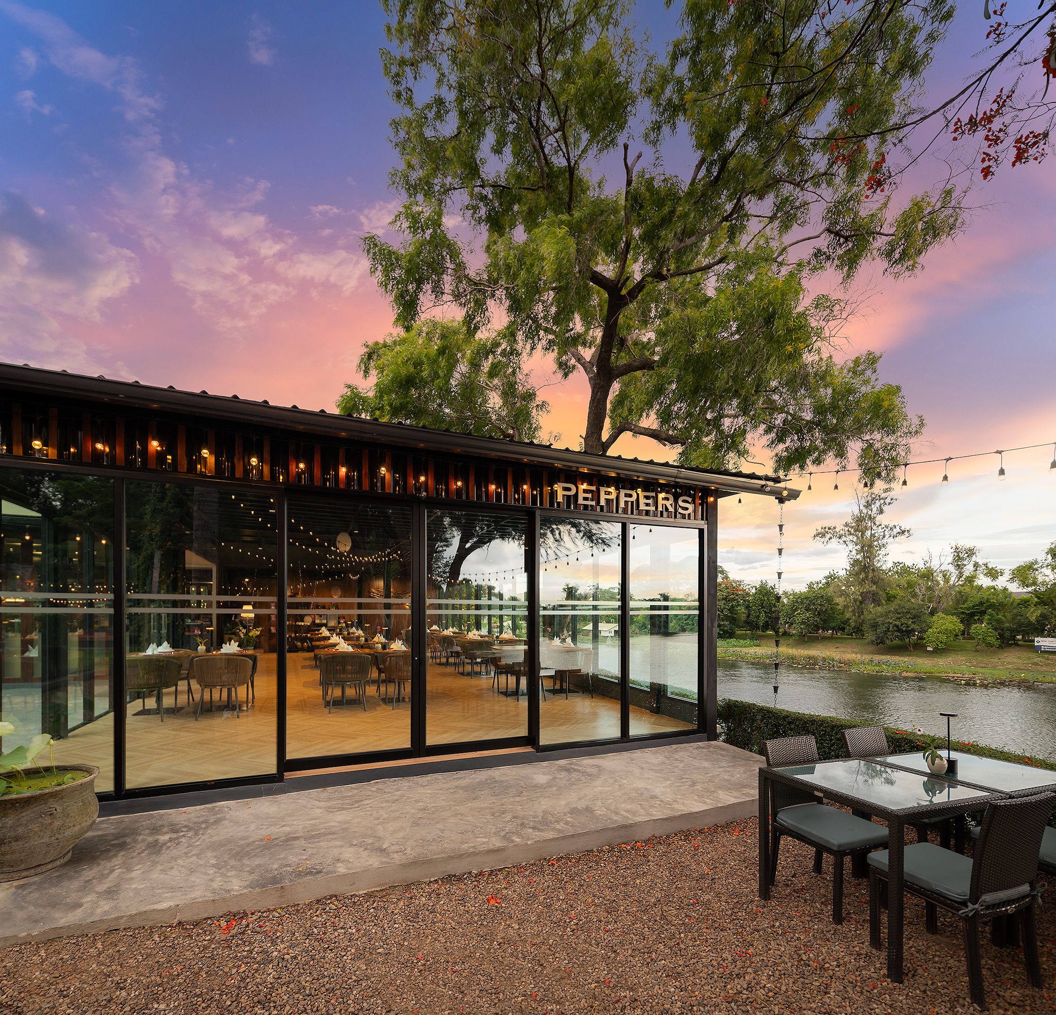 Restaurante com fachada de vidro, mesas ao ar livre e vista para a água.