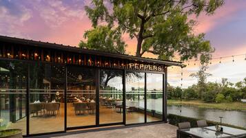 Restaurante com fachada de vidro, mesas ao ar livre e vista para a água.