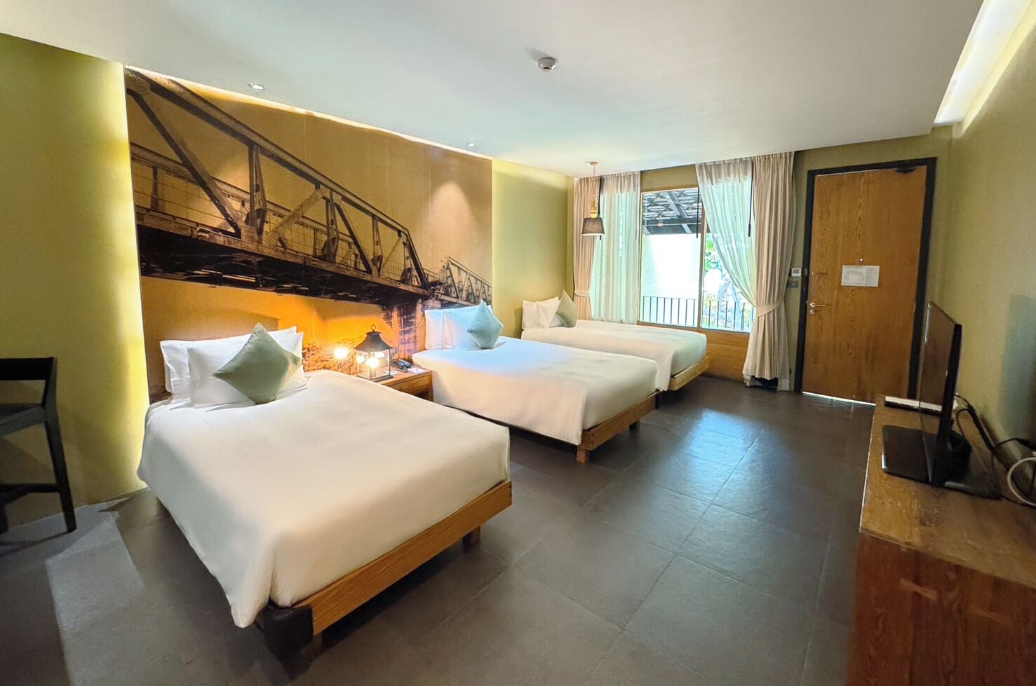 A hotel room with two beds, a desk, a chair, and a large window with curtains.