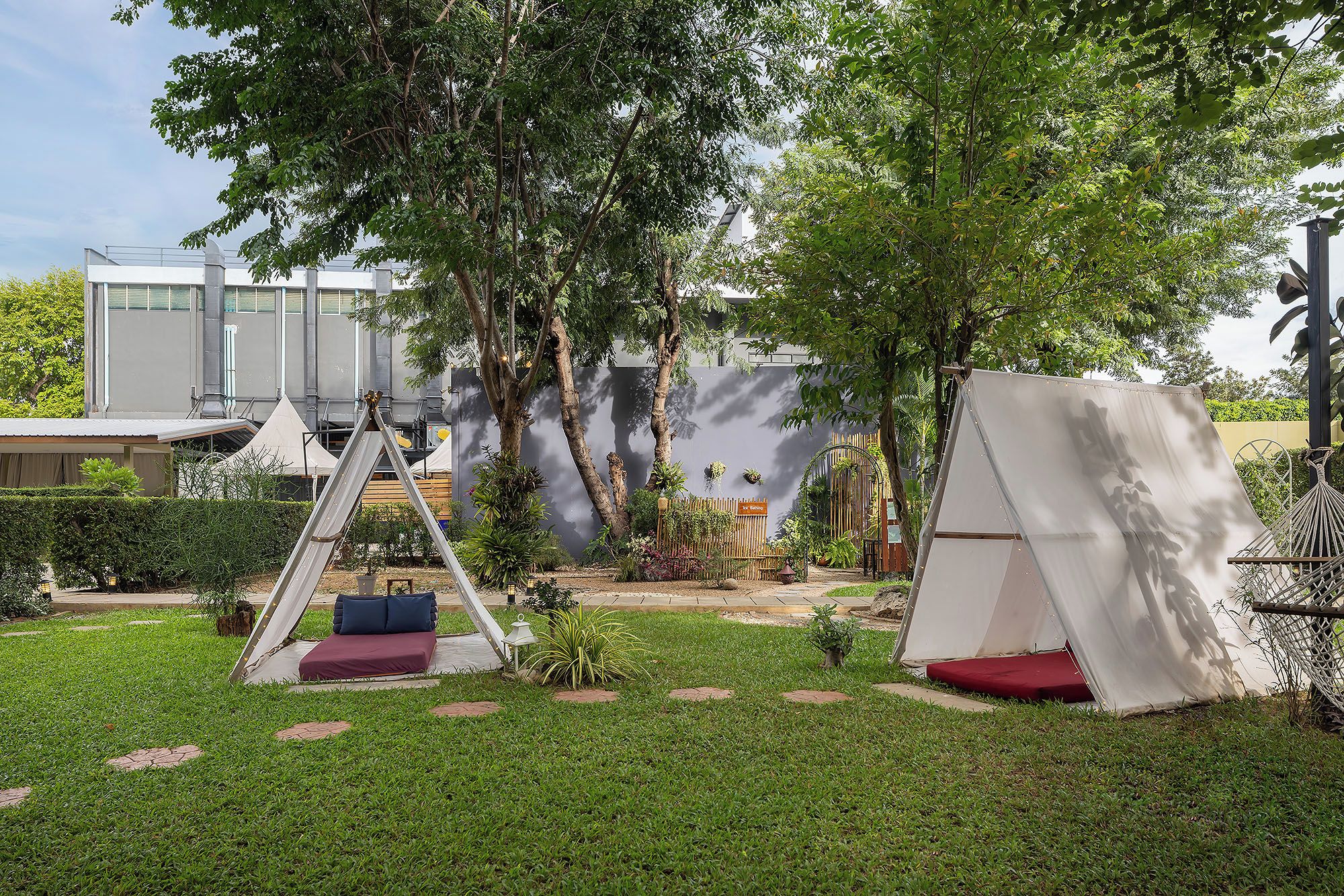 Un jardín con una estructura blanca similar a una carpa, una escalera y un pequeño rincón de estar con cojines.