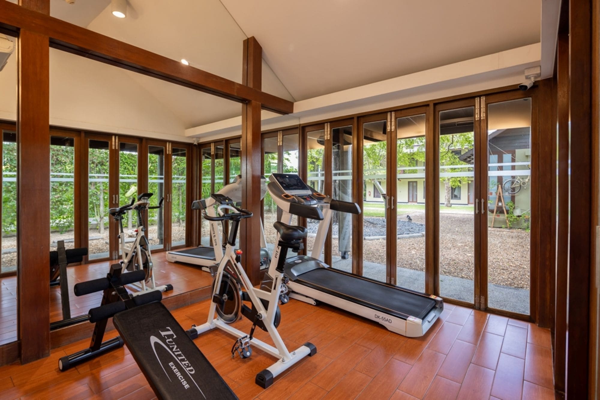 A gym with exercise equipment, large windows, and a wooden floor.