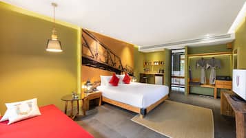 A hotel room with a bed, a red sofa, a small table with a lamp, and a TV.