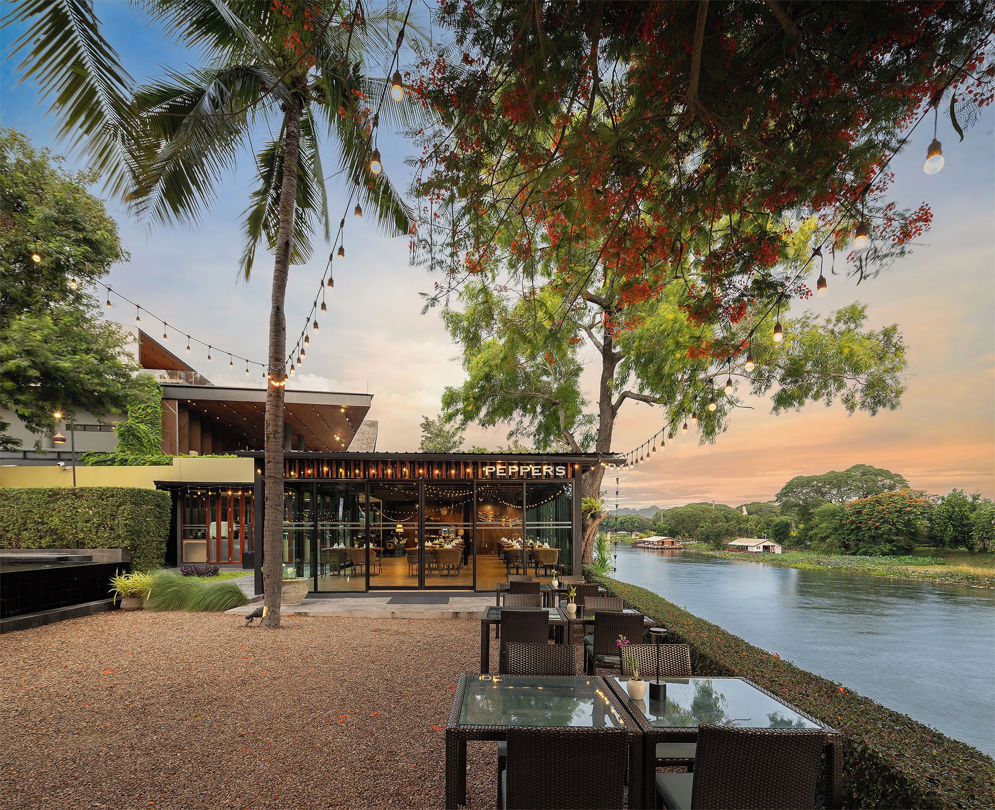 A restaurant with outdoor seating overlooking a body of water, featuring a modern design and string lights.