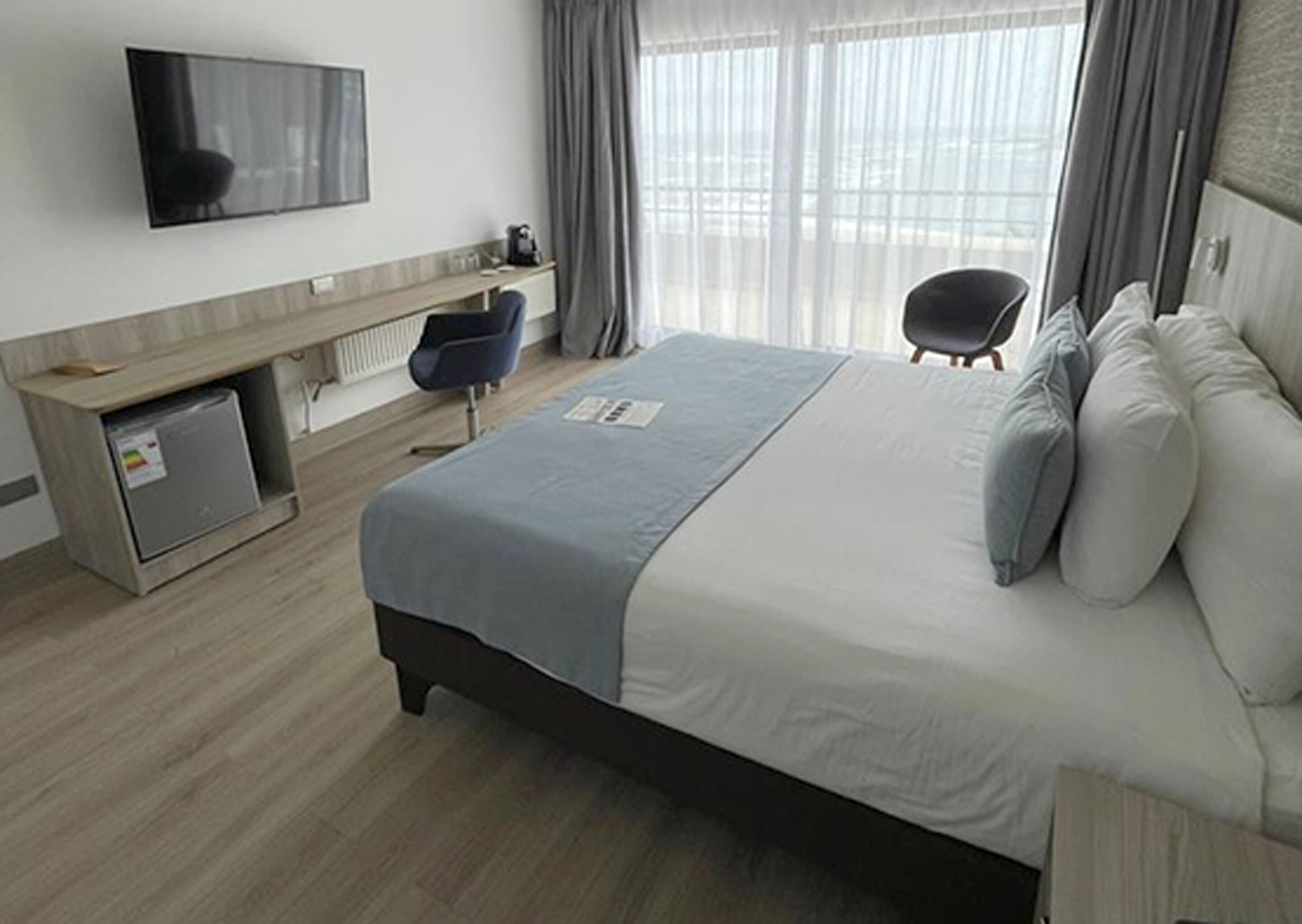 Ein Hotelzimmer mit Bett, Schreibtisch, Stuhl, Fernseher und einem Fenster mit Vorhängen.