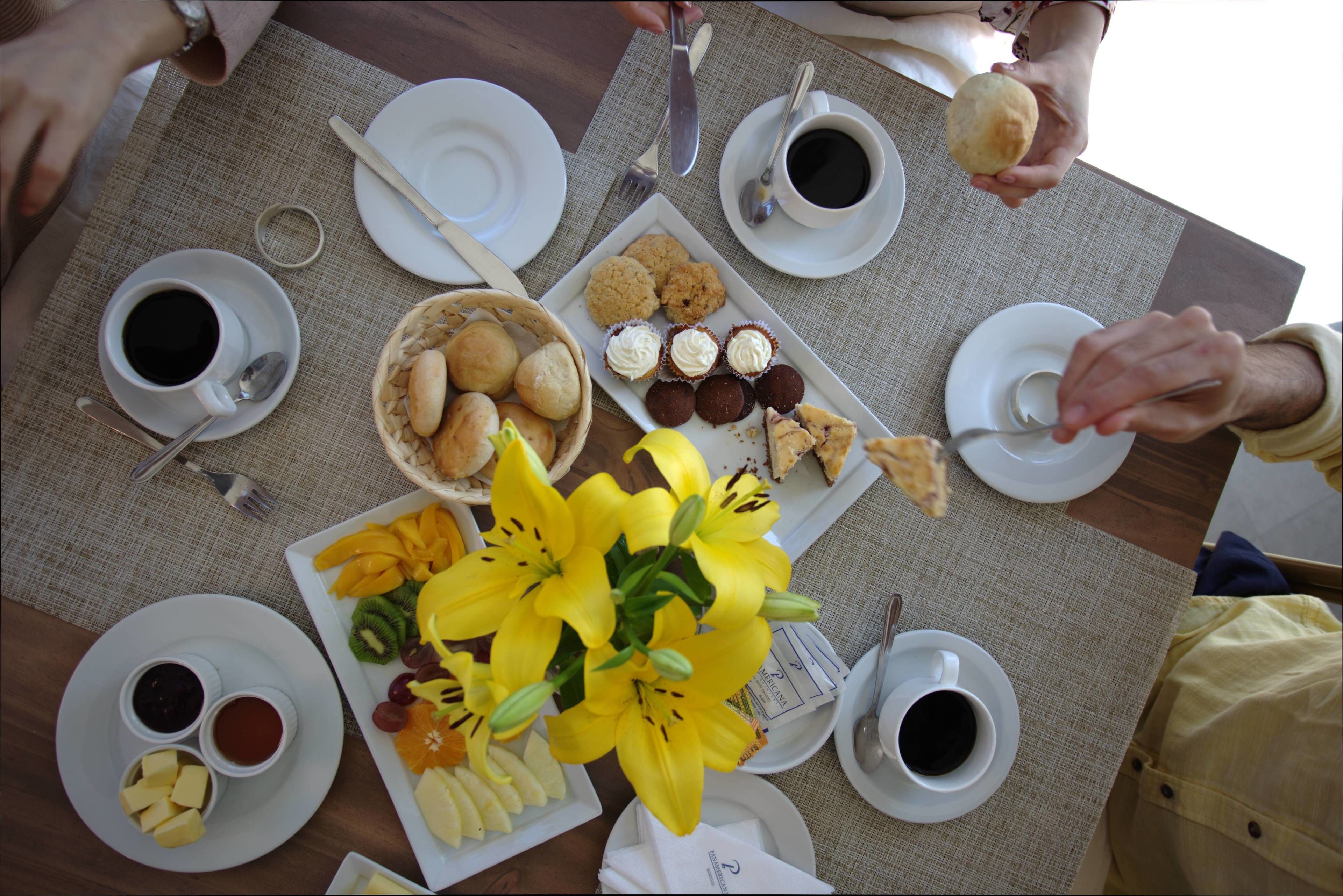 Een eettafel met borden eten, koffiekopjes en een boeket gele bloemen.