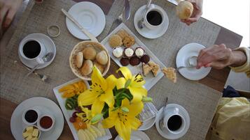 Een eettafel met borden eten, koffiekopjes en een boeket gele bloemen.