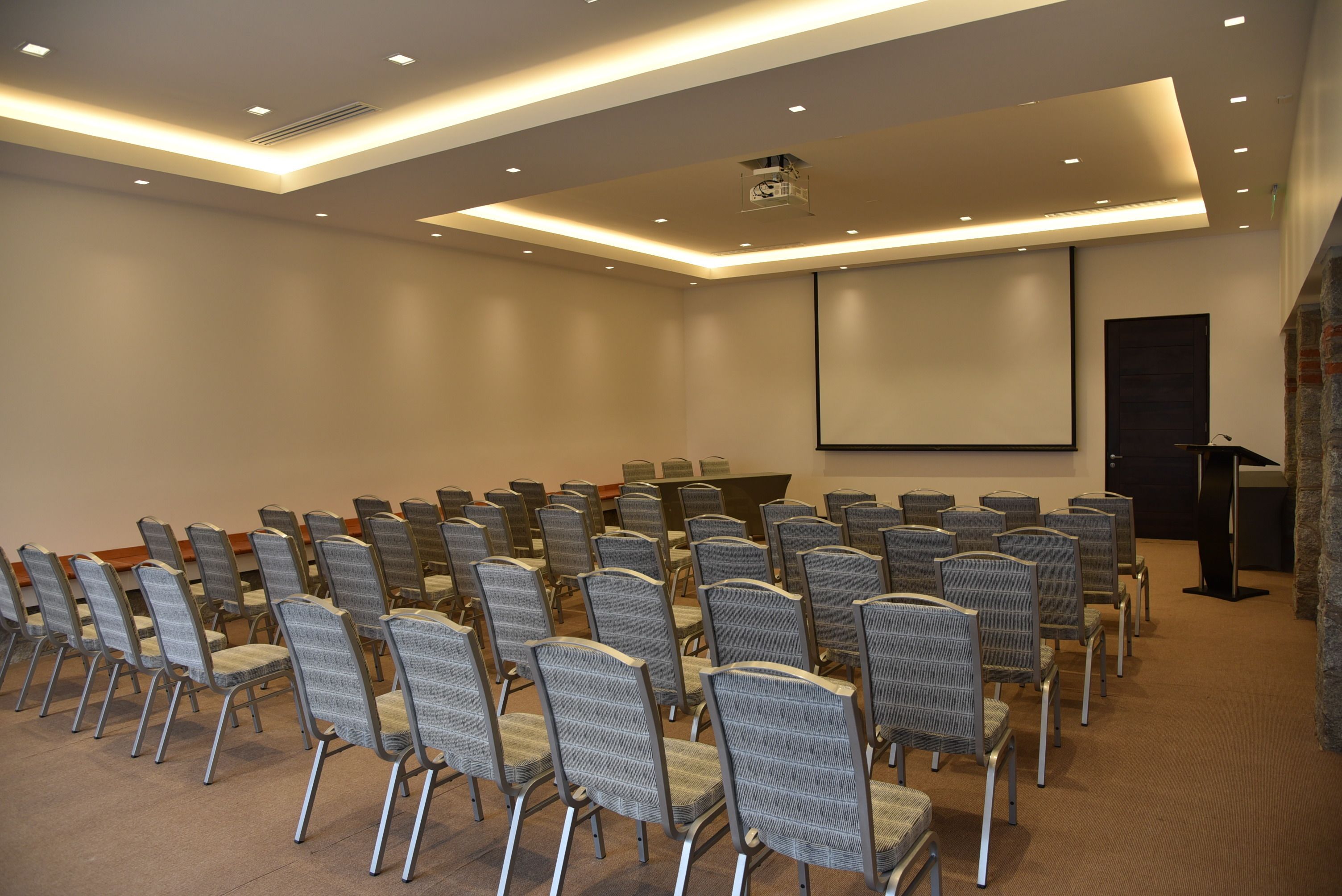 A conference room with rows of chairs, a projector screen, and a podium.