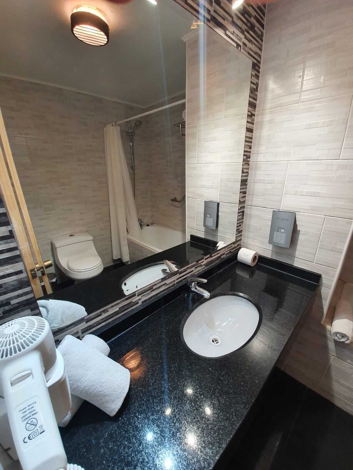 A modern bathroom with a black granite countertop, a white sink, a shower, and a toilet.