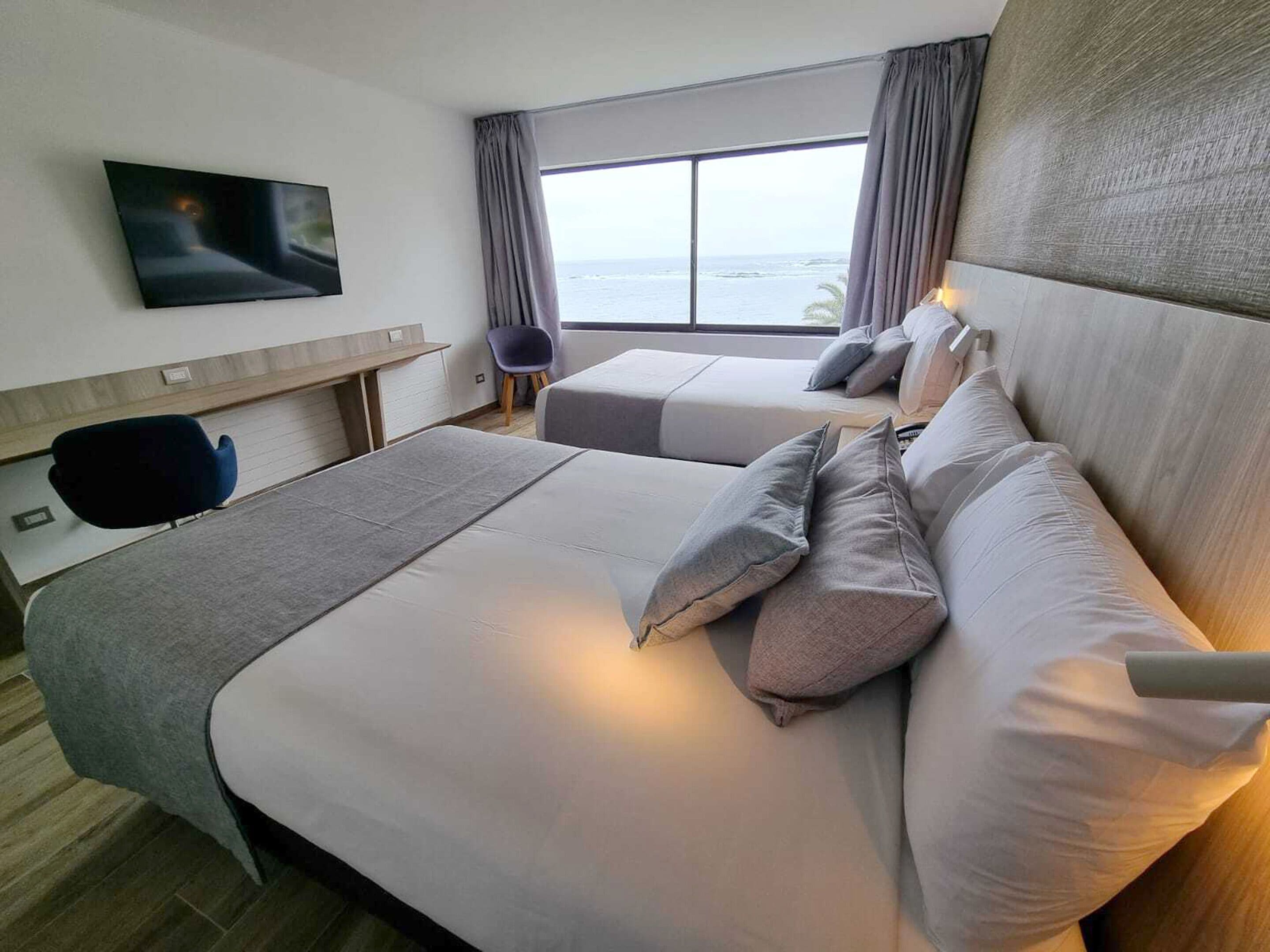 Una habitación de hotel con una cama grande, un escritorio, una silla y un televisor montado en la pared.