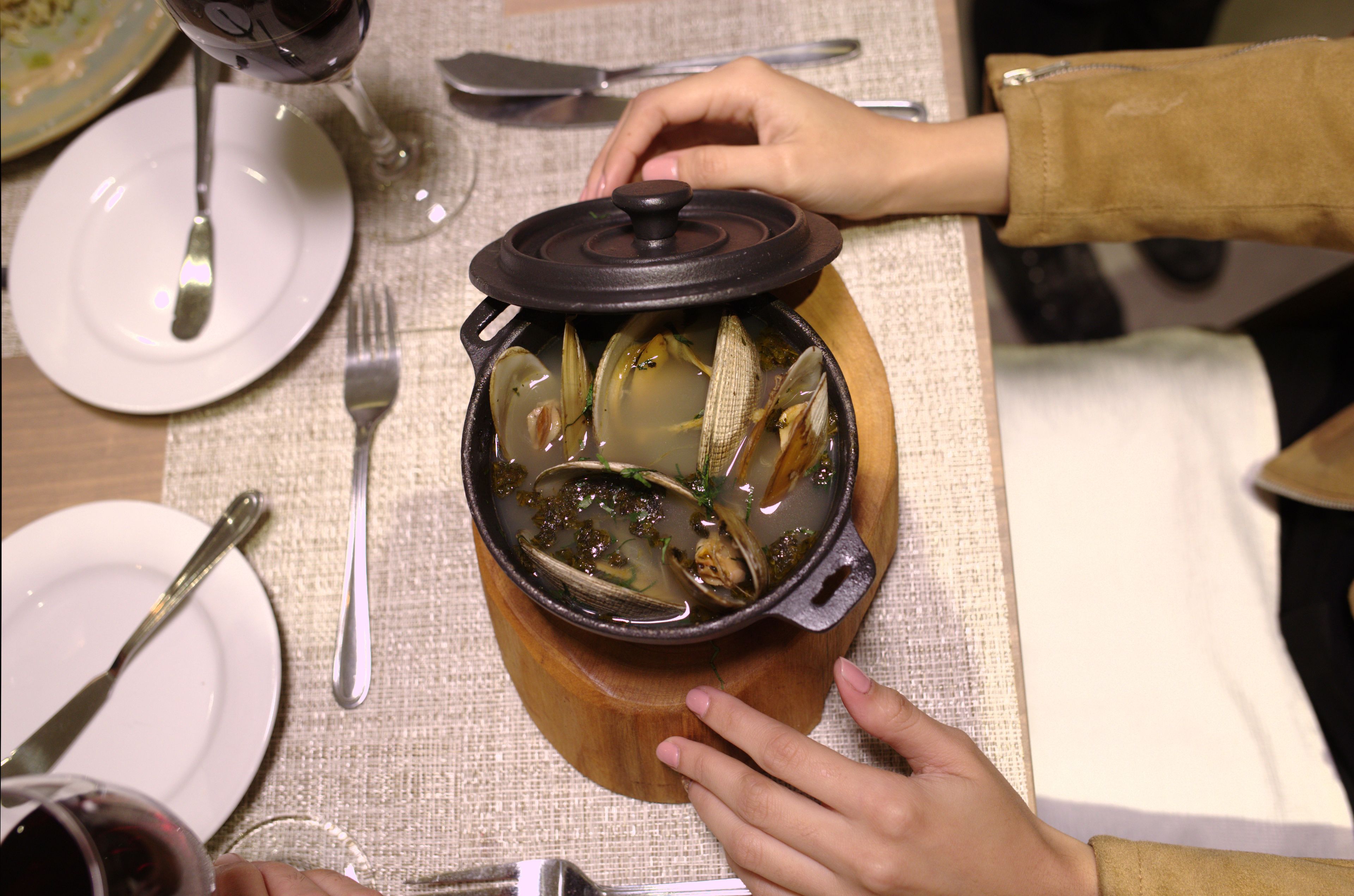 Una mesa de comedor con una olla de sopa, cubiertos y una copa de vino.