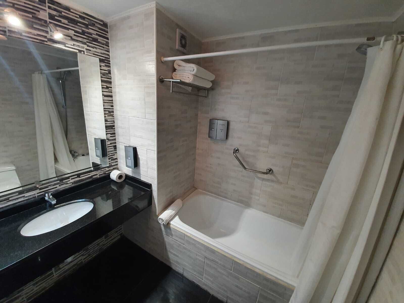 A modern bathroom with a black countertop, a white sink, a glass shower enclosure, and a white bathtub.