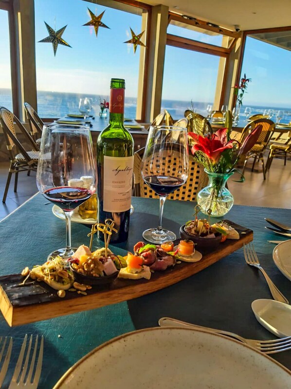 A dining table with a view of the sea, a bottle of wine, and a variety of appetizers. - Yachting Hotel Quintero (Quintero)