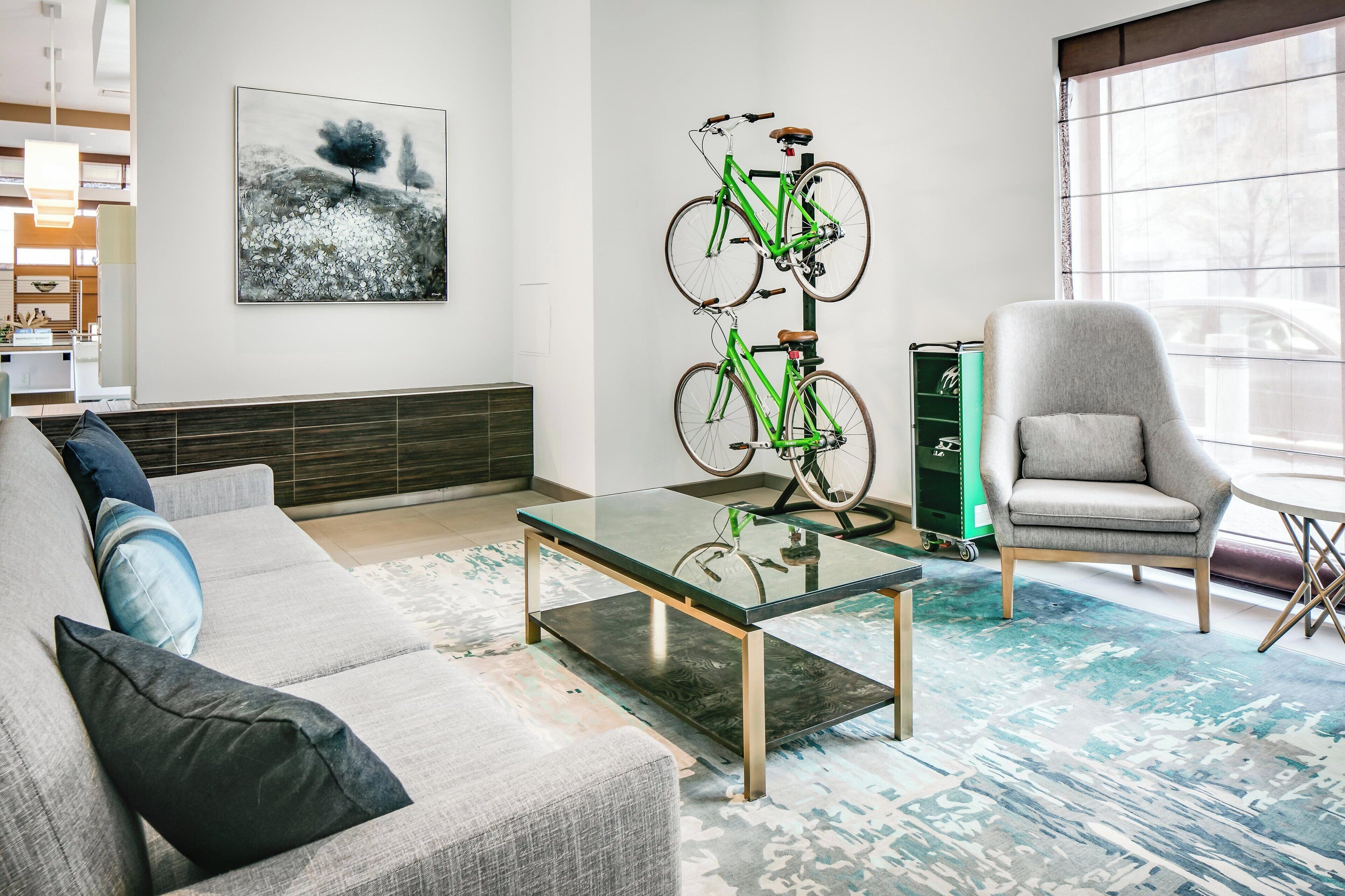 A modern living room with a sofa, a glass coffee table, a grey armchair, and a green bicycle mounted on a stand.