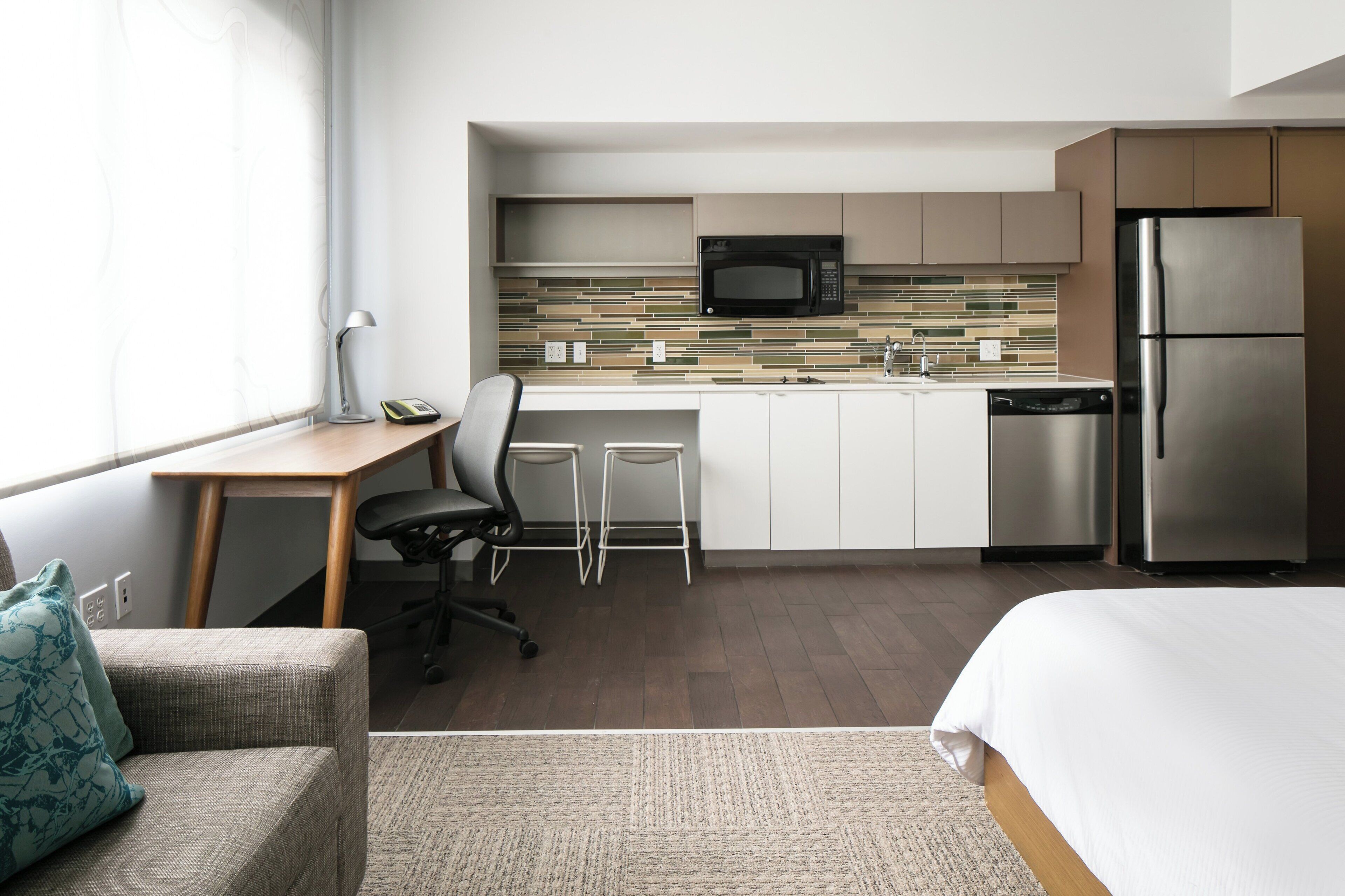 Een compacte hotelkamer met kitchenette, een bed, een bureau met stoel en een bank.