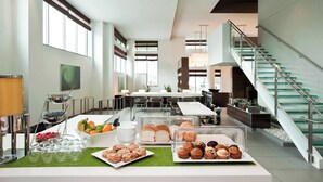 A modern hotel lobby with a buffet area featuring various pastries and fruits, a staircase, and a spacious seating area. - Element by Marriott Omaha Midtown Crossing (Omaha)