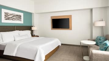 A hotel room with a large bed, a flat-screen TV, a small round table, and a sofa with cushions.