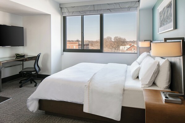 Une chambre d’hôtel équipée d’un lit, d’un bureau, d’une chaise, d’une télévision et d’une fenêtre donnant sur un paysage agréable.