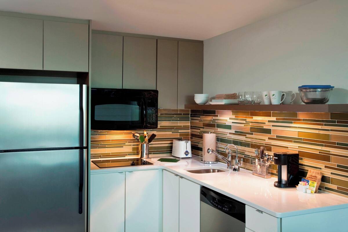 Una cocina moderna con un refrigerador de acero inoxidable, un microondas, una cafetera y un lavabo.
