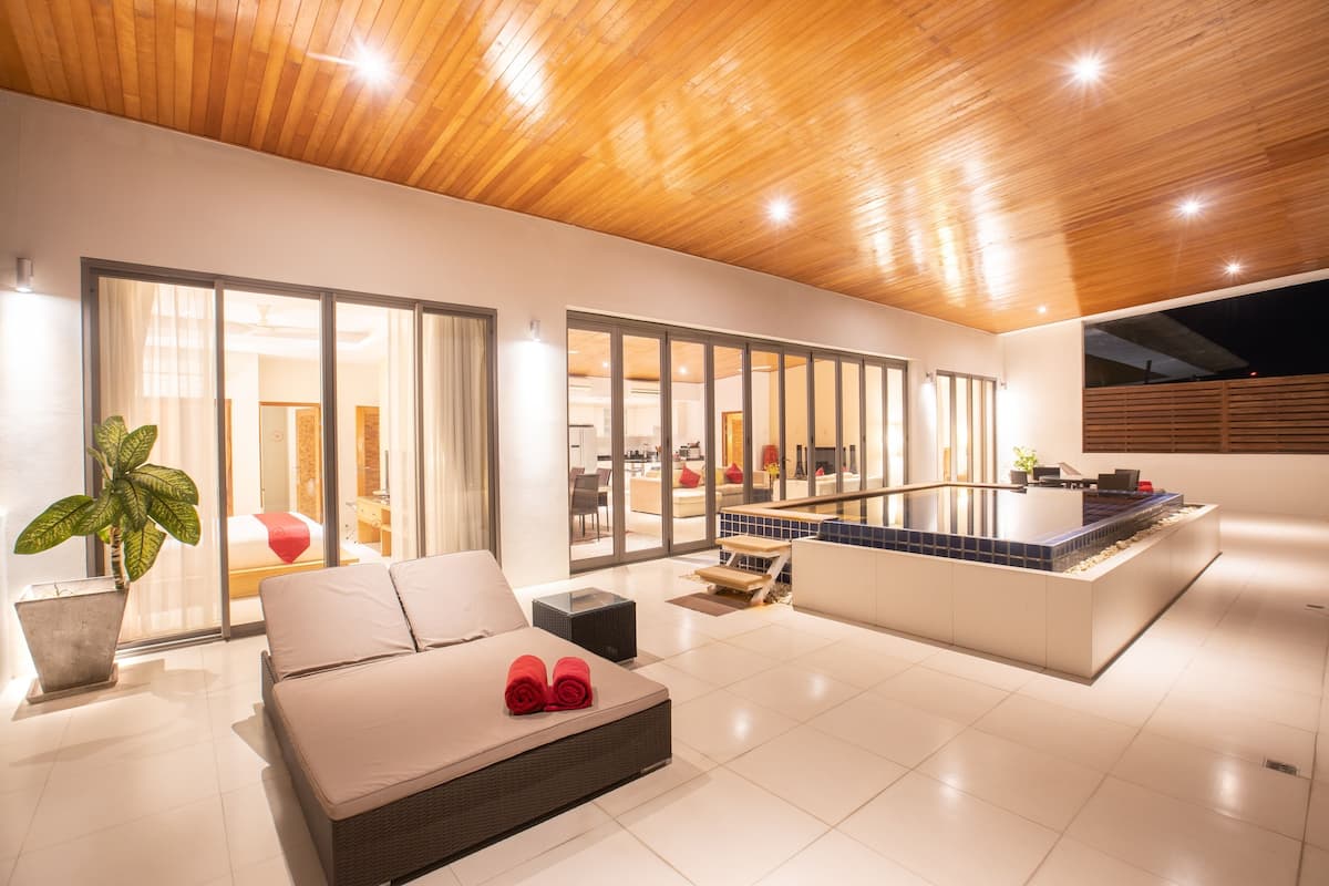 A modern hotel room with a large bed, a small table, and a seating area with a view of the pool and outdoor space.