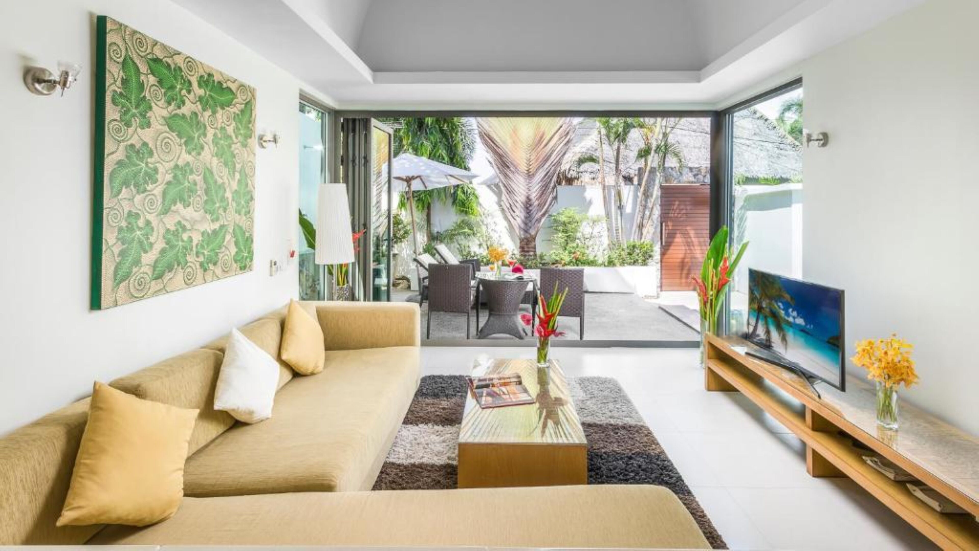 A modern living room with a sofa, coffee table, and TV, with a view of an outdoor patio area.