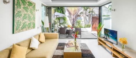 A modern living room with a sofa, coffee table, and TV, with a view of an outdoor patio area.
