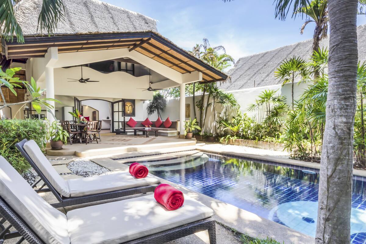 A pool area with lounge chairs and a covered seating area with a table and chairs.