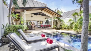 Un área de piscina con sillones de descanso y una zona de estar cubierta con mesa y sillas.