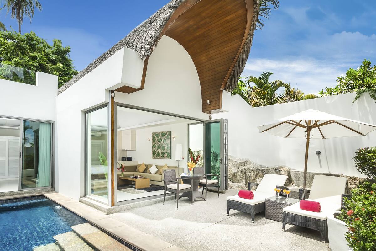 A modern villa with a glass-enclosed pool, outdoor seating area, and a thatched roof structure.