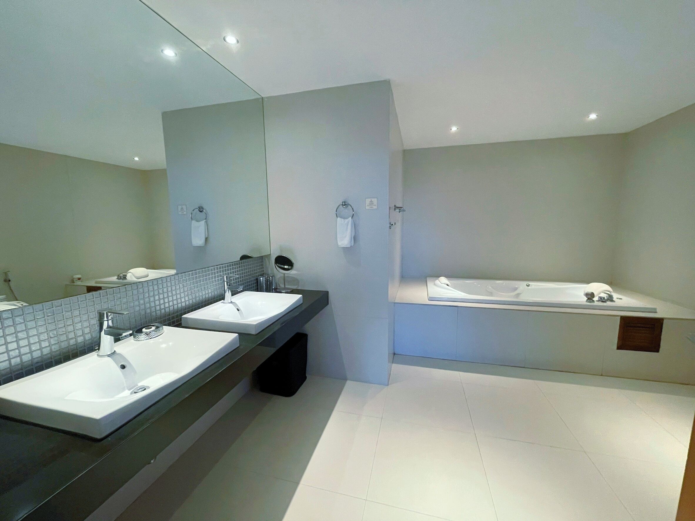 A modern bathroom with two sinks, a large mirror, and a separate bathtub area.