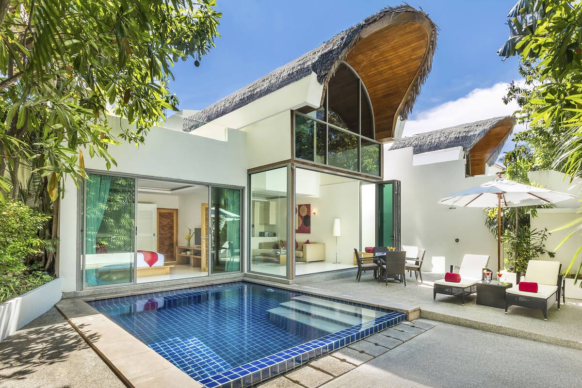A modern house with a swimming pool, glass doors, and a thatched roof.