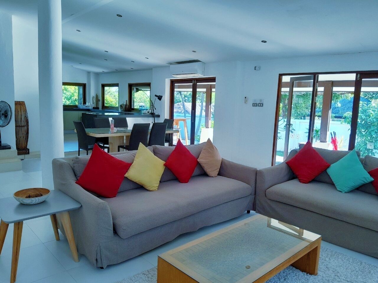 A modern living room with a grey sofa, a small table, and a coffee table. There is a dining area in the background with a table and chairs.